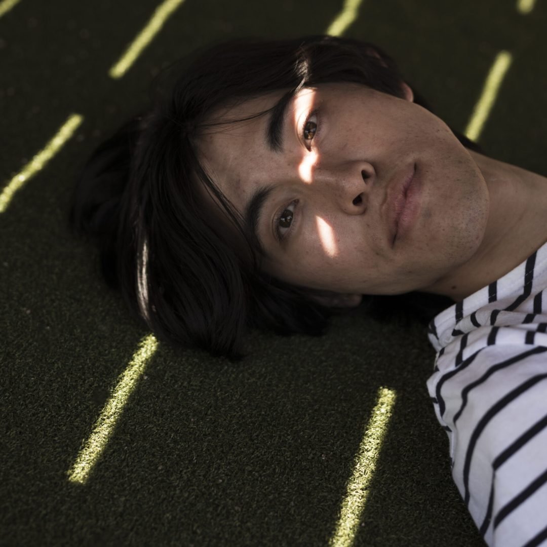 young-asian-male-looking-camera-while-lying-shadow